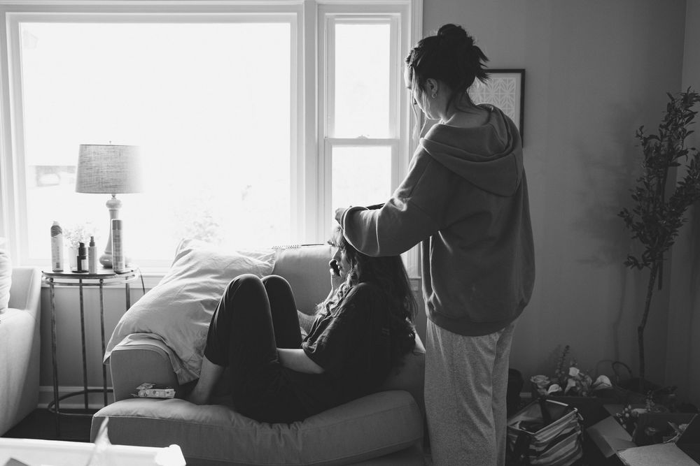 Black and white photo of two people sharing a tender moment by a sunlit window in a cozy living room.