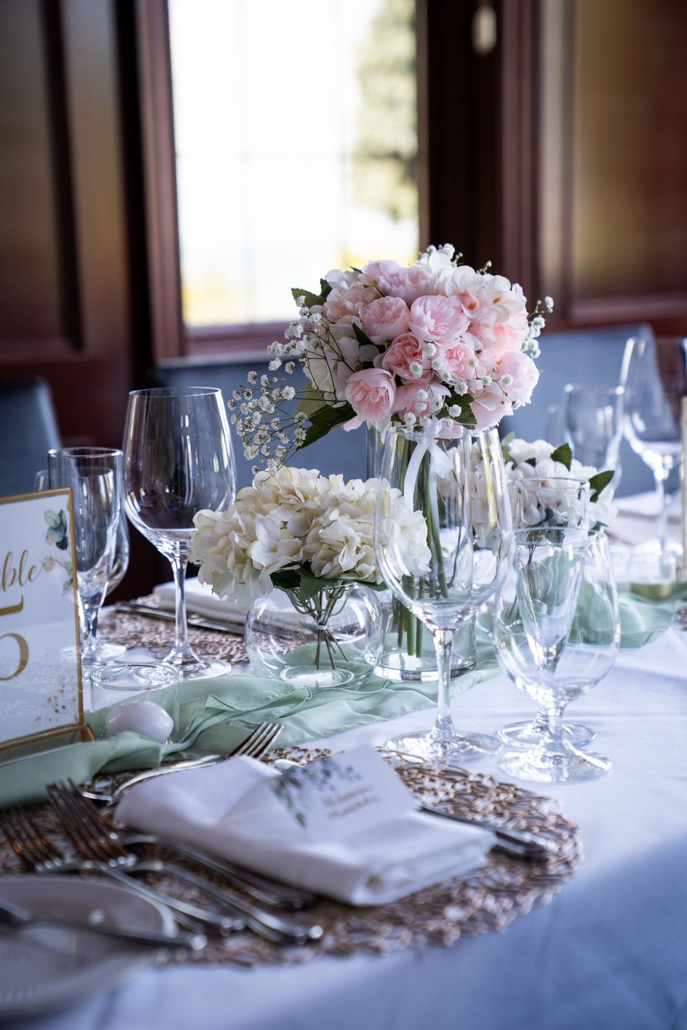 An elegant wedding table setting with pink and white floral centerpieces and crystal glasses.