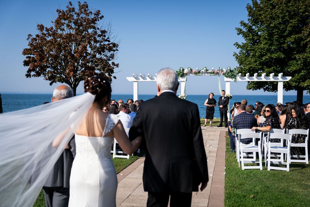 A wedding ceremony being held at an outdoor waterfront venue with a white pergola and chairs set up for guests.