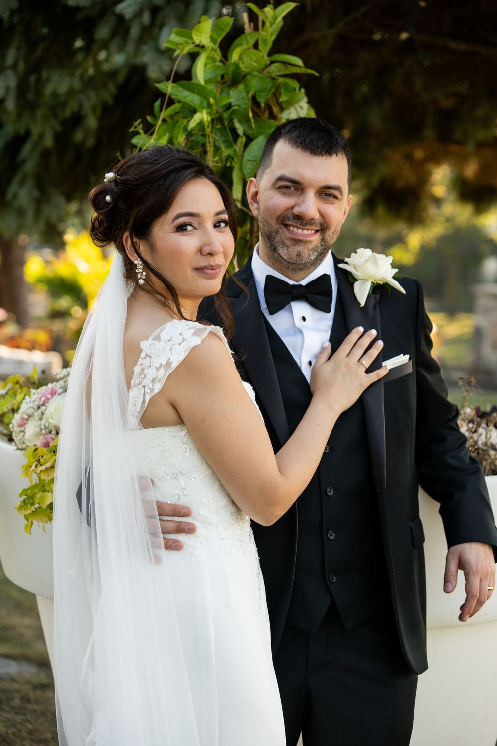A wedding couple stands together in formal attire against a garden background.