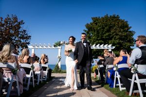 Newlyweds walk down the aisle at an outdoor waterfront ceremony under blue skies.