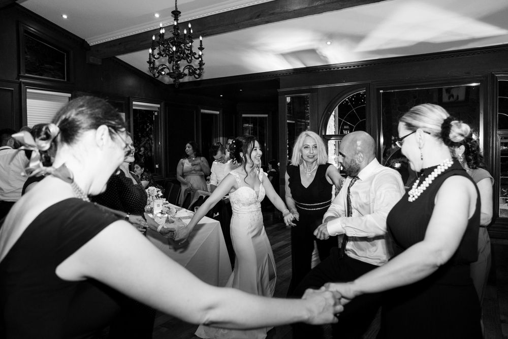 Black and white photo of wedding guests dancing in a circle during the reception.