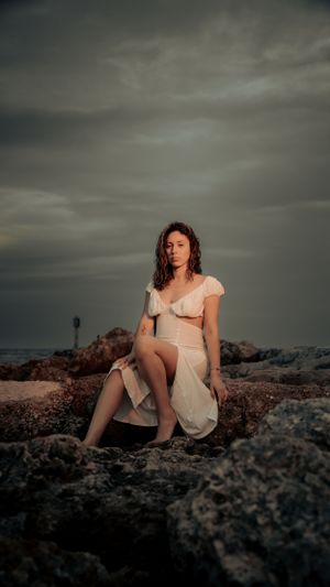 Sunset portrait on rocky coastline wearing white two-piece dress.