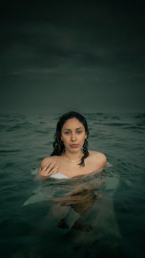 Moody ocean portrait with wet hair emerging from dark teal waters.
