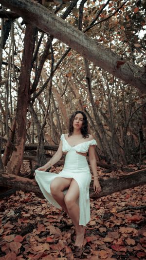 Ethereal fashion portrait in a white dress among autumn trees and fallen leaves.