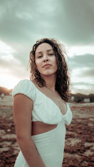 Dramatic portrait in white dress against cloudy sky and desert landscape.