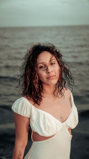 Beachside portrait featuring wet curly hair and white cutout dress against moody ocean backdrop.