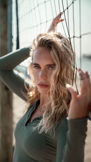 Artistic portrait against volleyball net with natural lighting and dramatic shadows.