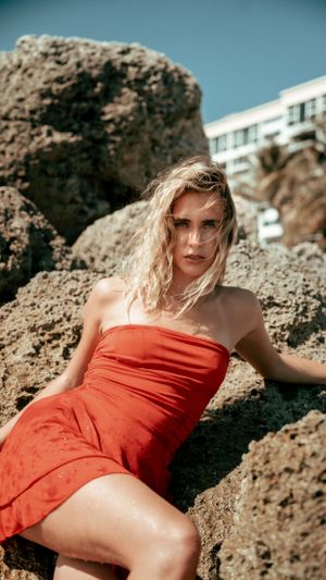 Fashion photo shoot with red dress against rocky coastal backdrop.