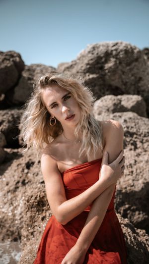 Portrait in red dress posed among coastal rocks with soft lighting.