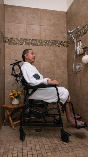 Person in white robe seated in wheelchair in a modern tiled bathroom with mosaic accents.