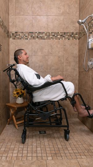 Profile view of person in wheelchair wearing white robe in accessible bathroom setting.