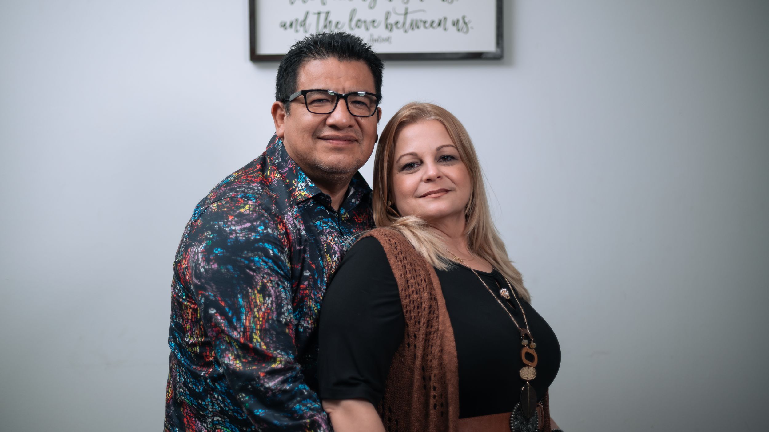 A couple poses together indoors wearing contrasting dark and light clothing.