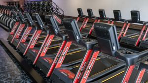 Row of red and black treadmills in an empty fitness center.