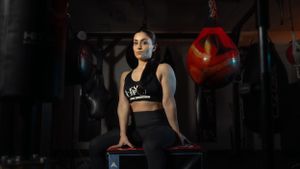 Athletic woman in black workout attire sits on fitness equipment in a dimly lit gym setting.