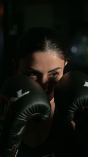 Close-up shot of eyes peeking over black boxing gloves in dramatic lighting.
