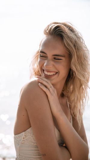 Woman with tousled blonde hair laughs joyfully on sunny beach.