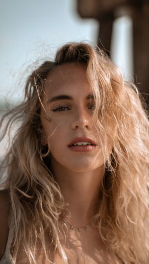 Close up portrait of woman with windswept blonde hair wearing delicate necklace.