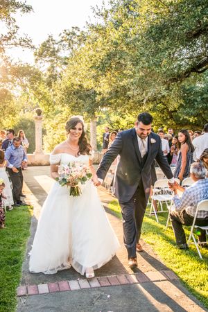 Newlyweds walking down the aisle while wedding guests celebrate in an outdoor garden setting.