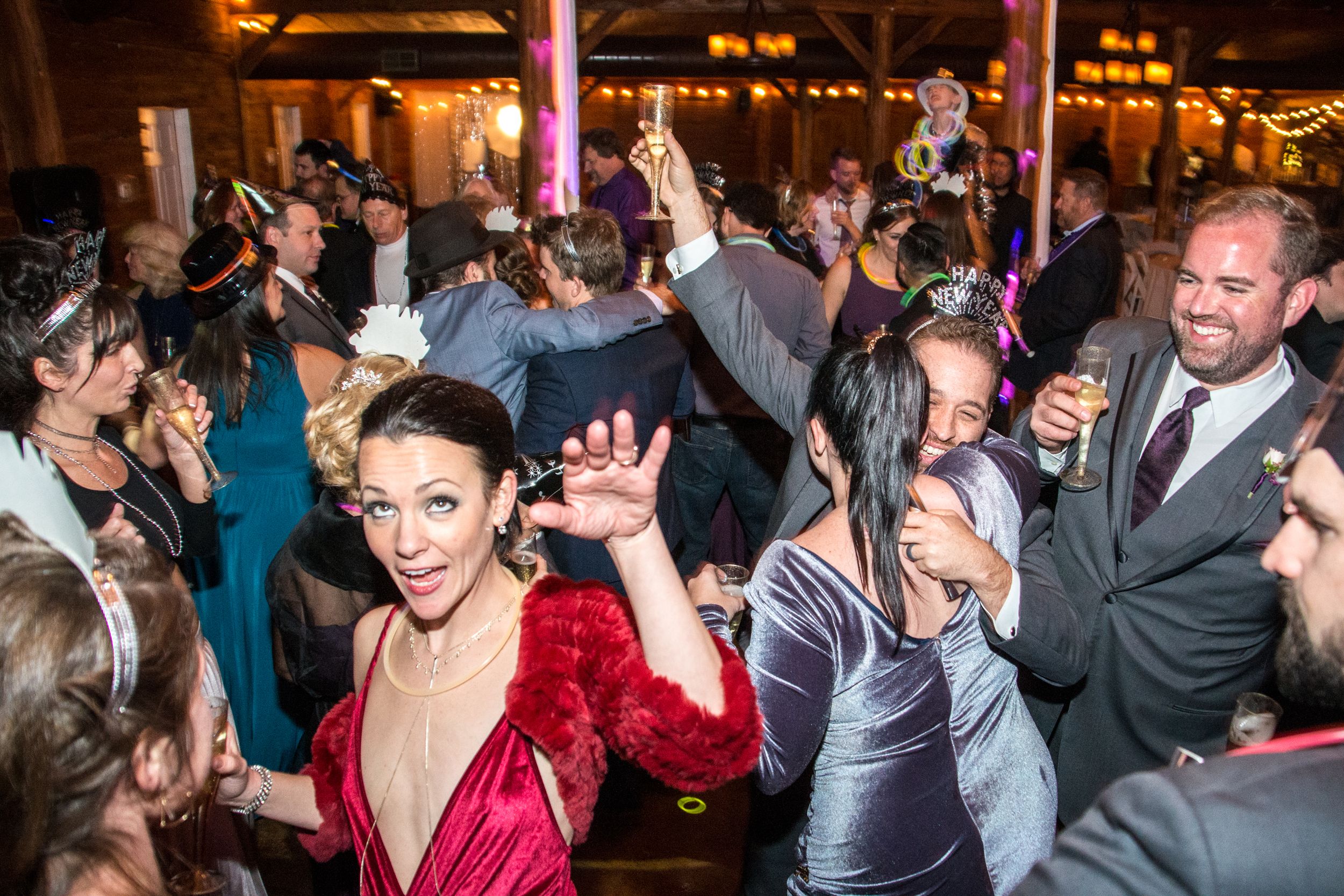 Guests dancing and celebrating at a lively indoor party event with drinks and festive attire.