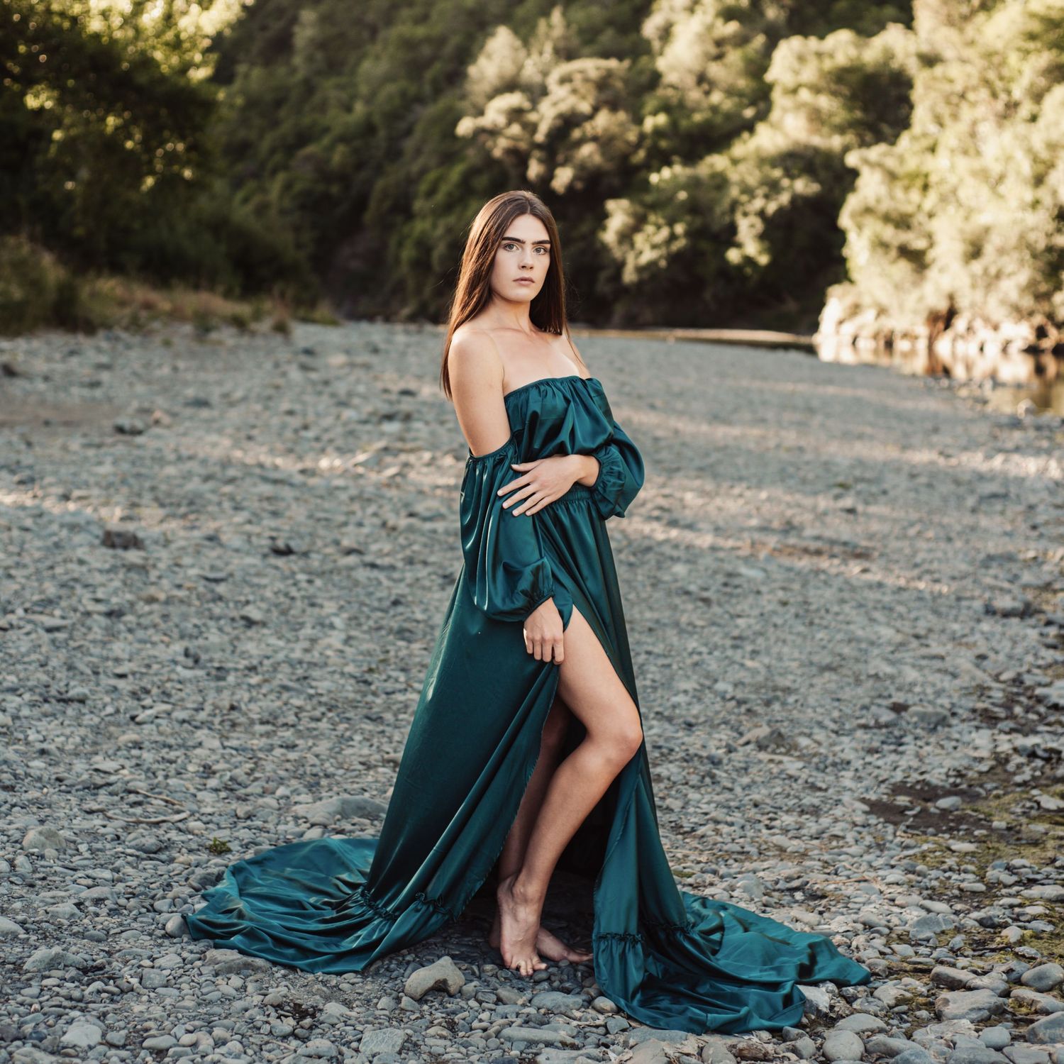 Elegant teal dress sweeps across rocky shoreline in artistic portrait.