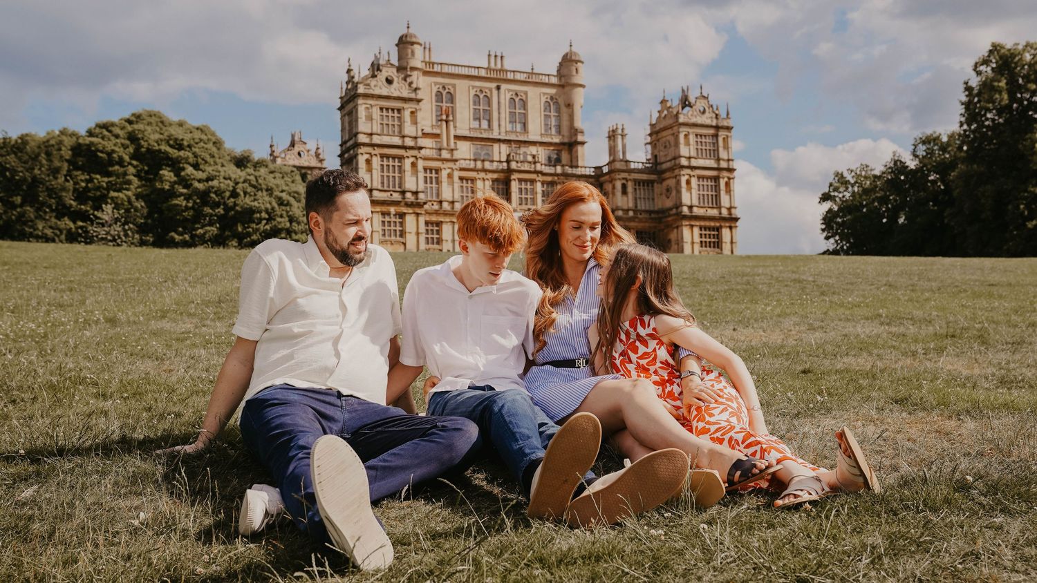 Family relaxing on grass with historic mansion building in background.