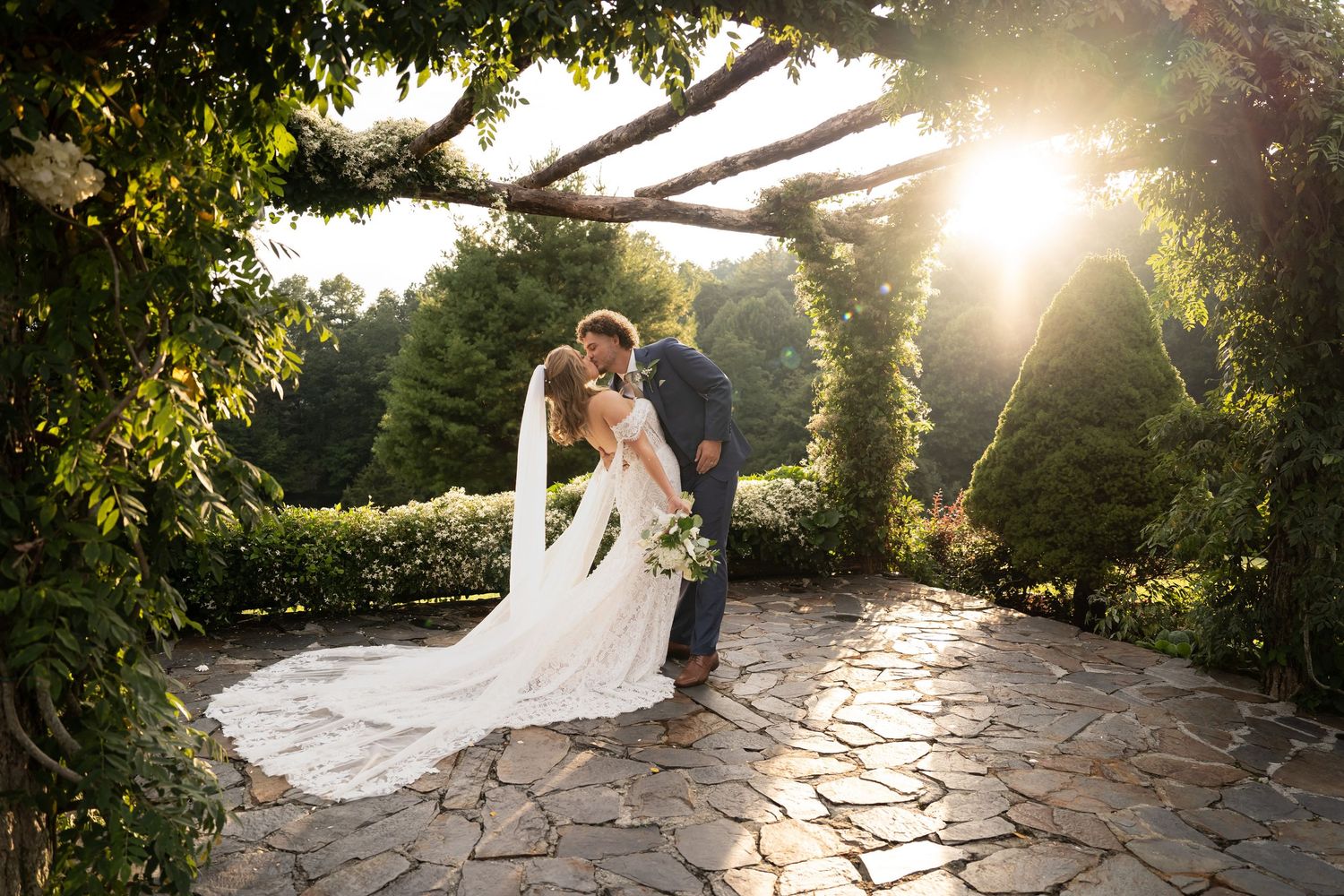 A romantic wedding couple embraces under a lush garden arch during an outdoor ceremony. Leavenworth, WA