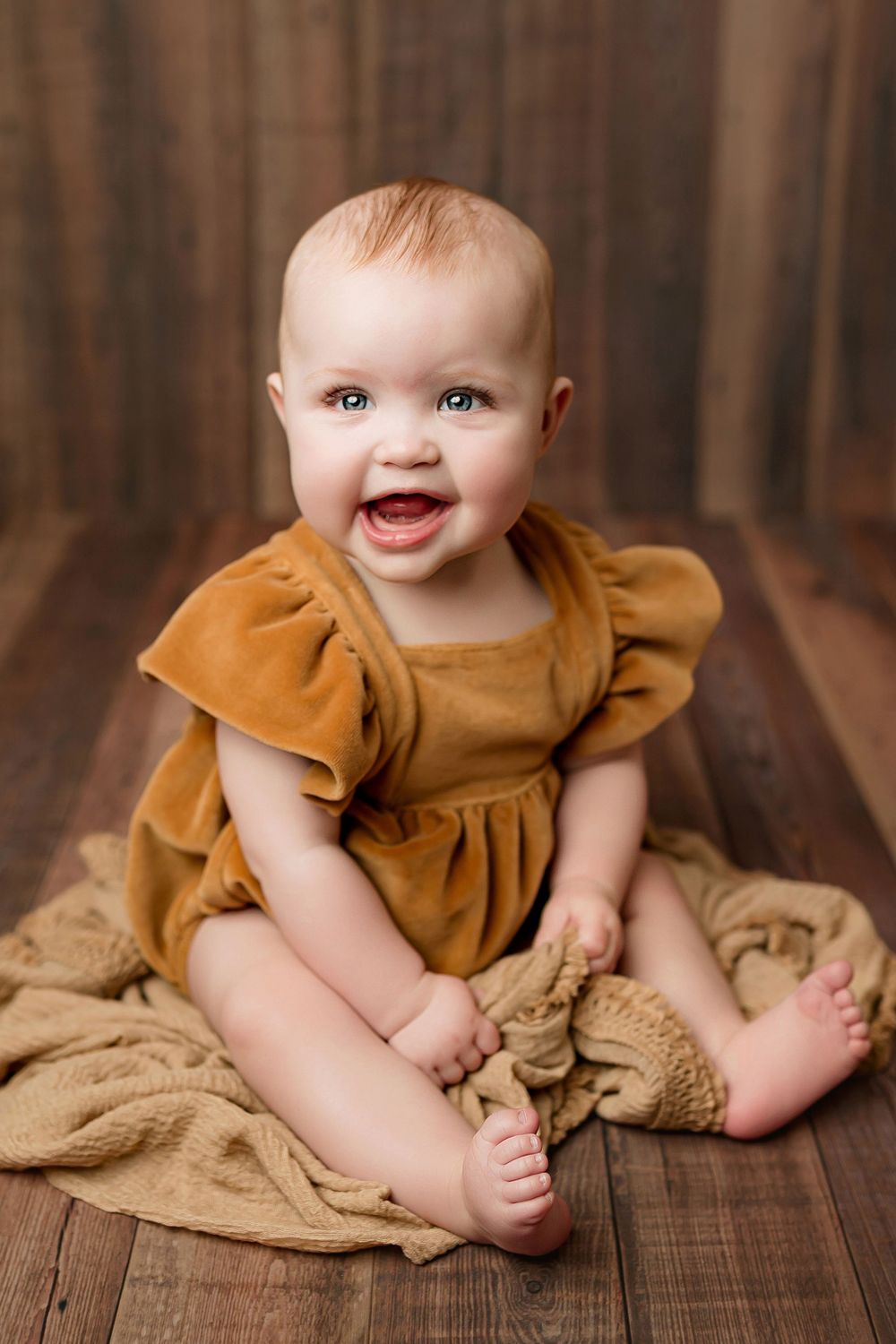 Laughing baby girl in gold velvet ruffle dress sitting on rustic wood floor during milestone session at Flowertown Photography  Summerville