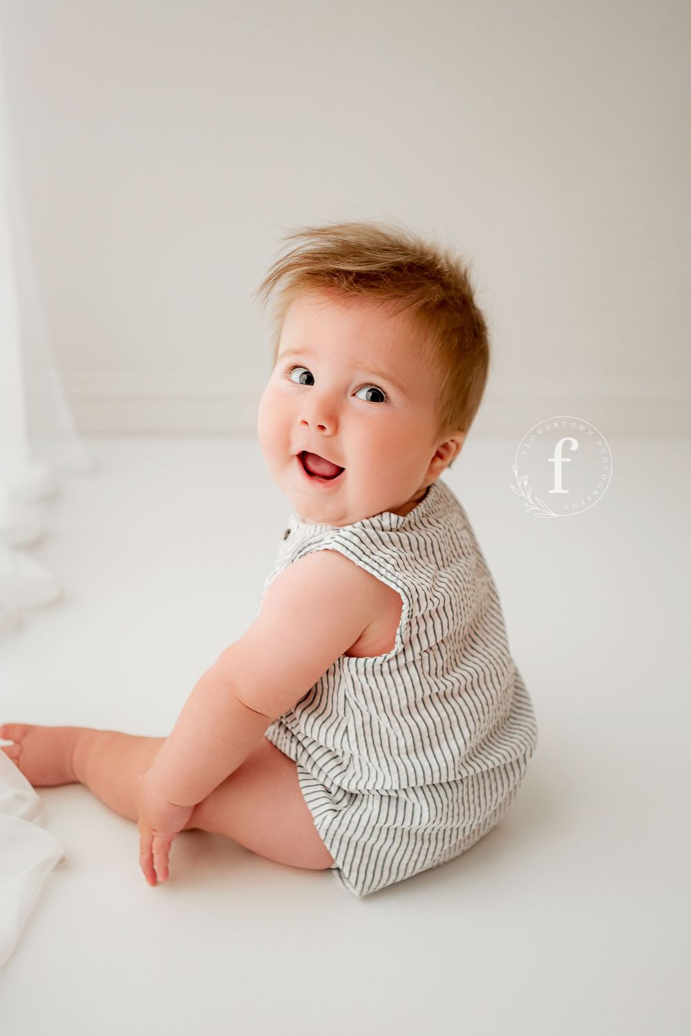 Happy baby boy in gray striped romper looking over shoulder and smiling during sitter session at Flowertown Photography Summerville SC