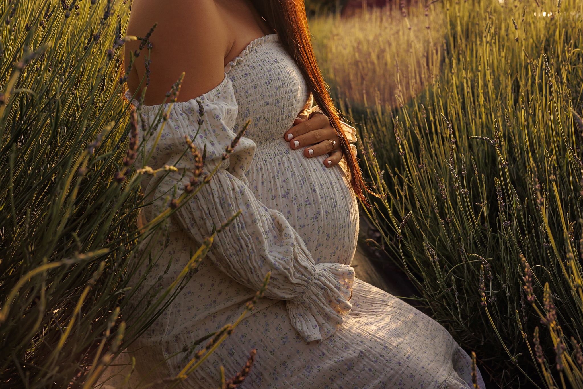 Person in white dress poses among tall grass and wildflowers at sunset.