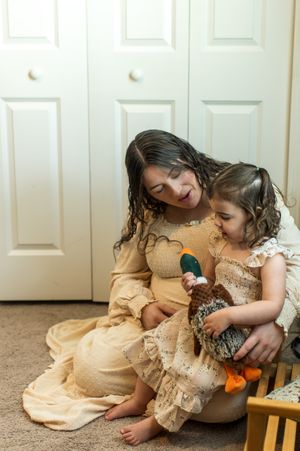 A woman and young girl in matching tan dresses sit on the floor together playing with a stuffed duck toy.