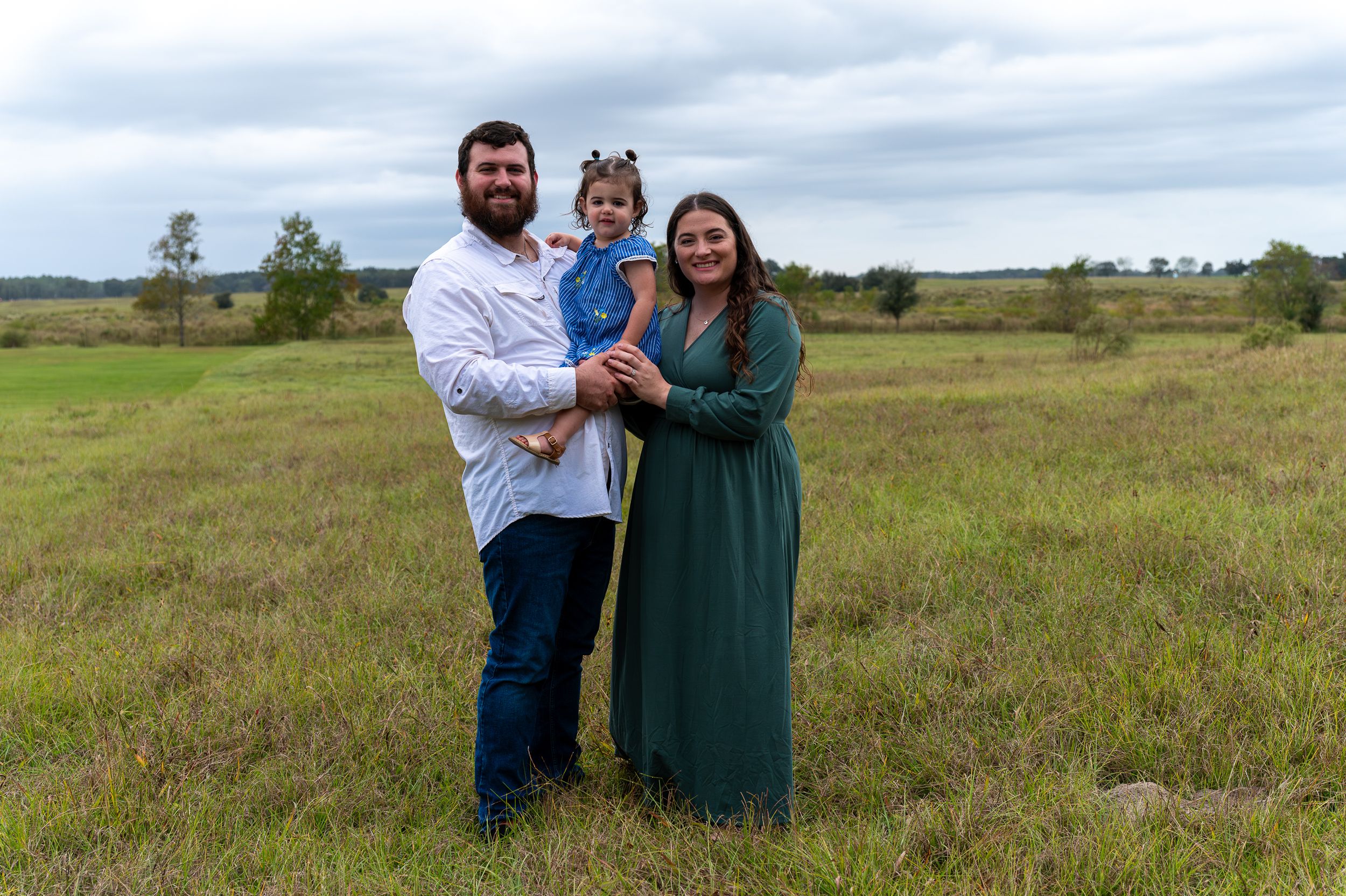 A family stands together in a green grassy field on an overcast day.