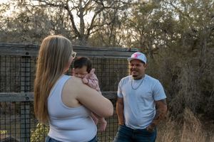 A couple with a baby enjoying an outdoor moment near a metal fence surrounded by trees.