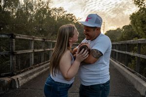 Couple sharing a tender moment on a bridge at golden hour, surrounded by lush greenery and warm sunset light.