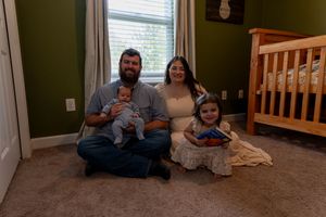 Family of four poses in nursery room with crib, parents sitting on floor holding two young children.