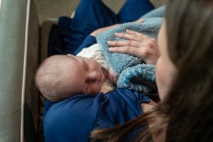 Mother breastfeeding newborn baby wrapped in blue blanket, infant nursing in mothers arms.