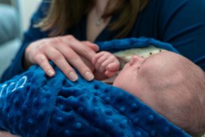 Newborn baby wrapped in blue blanket held by mother, gently grasping her finger in a tender moment.