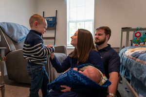 Family with newborn baby, mother holding infant while toddler son interacts in a cozy nursery bedroom.