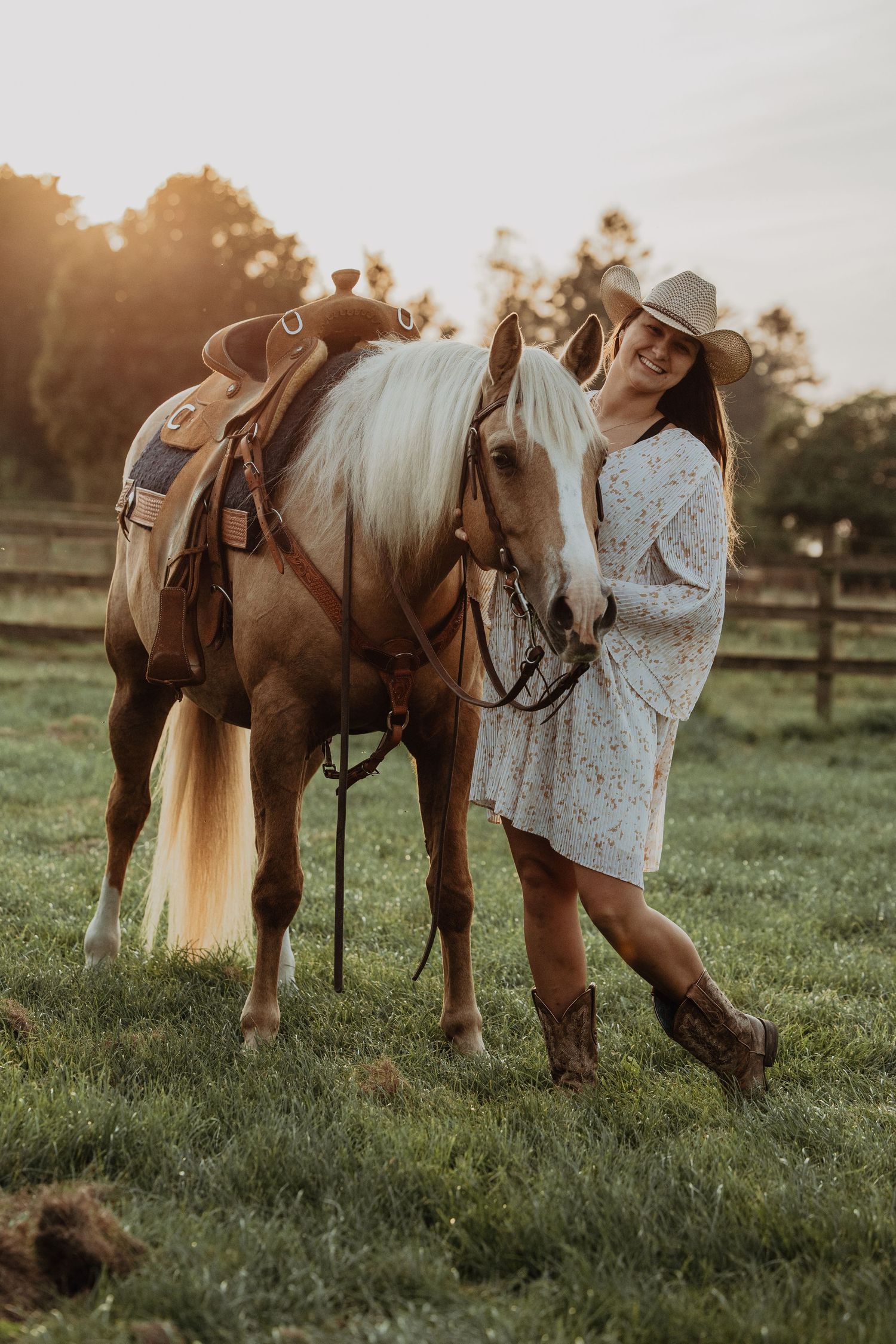 A horse and rider pose together in a sunlit field at sunset wearing country western attire.
