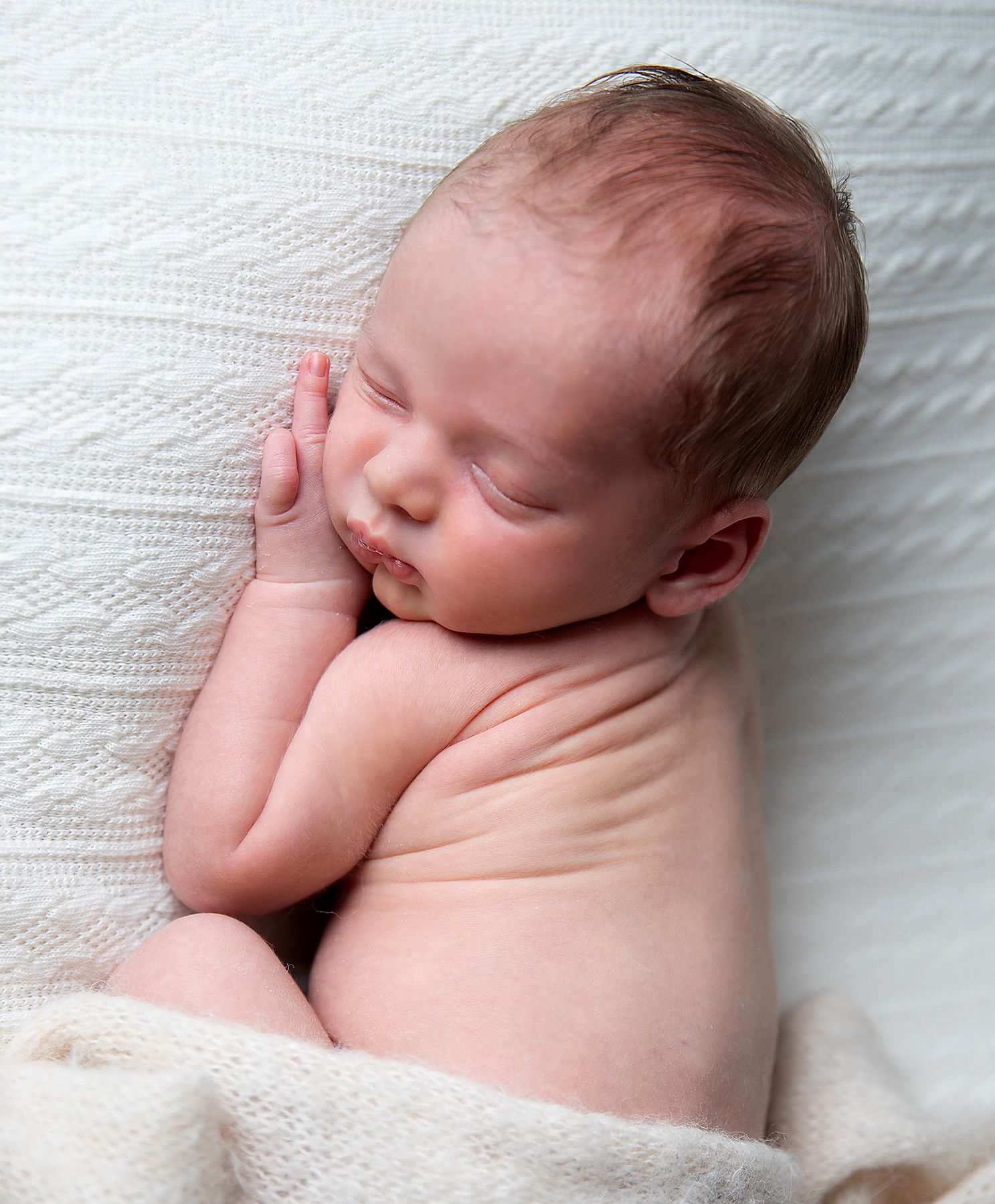 Peaceful sleeping newborn baby lying on soft white knitted blanket in natural light. During a newborn photoshoot in Bexley