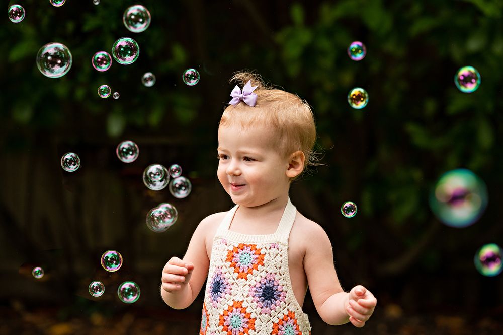 Toddler in floral outfit playing with soap bubbles outdoors.