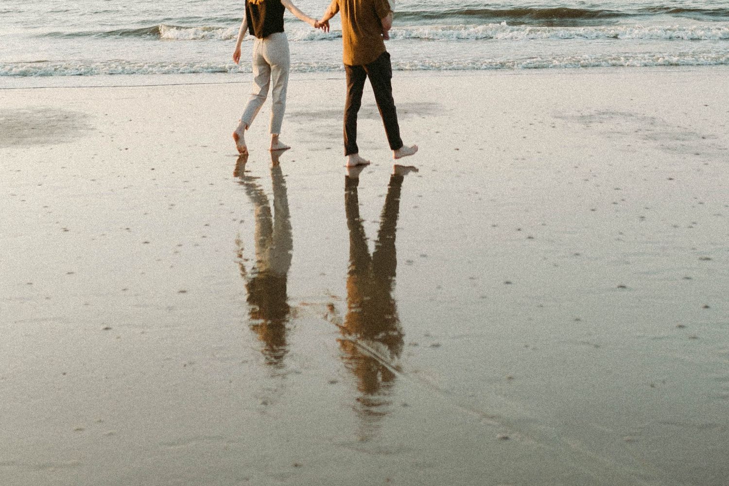 Photo by B. Logsdon of a couple walking on wet sand at the Hilton Head beach with their reflections mirrored in the shallow water.