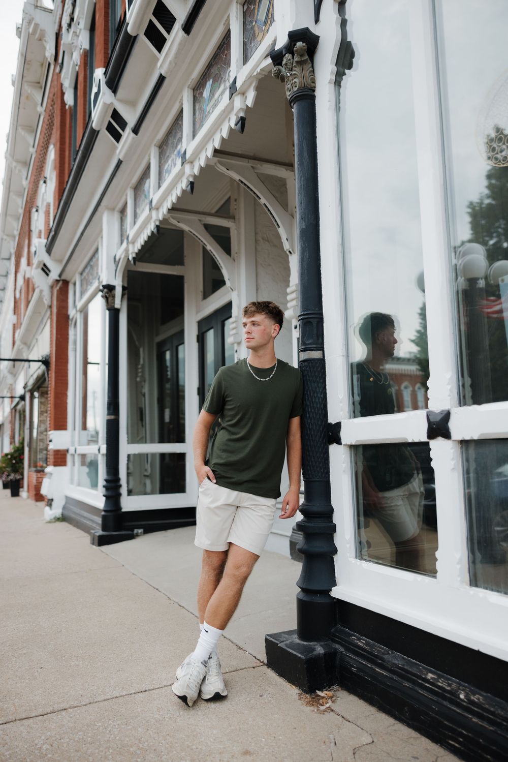 Person in green t-shirt and white shorts walking past white storefronts with black trim on a sidewalk.