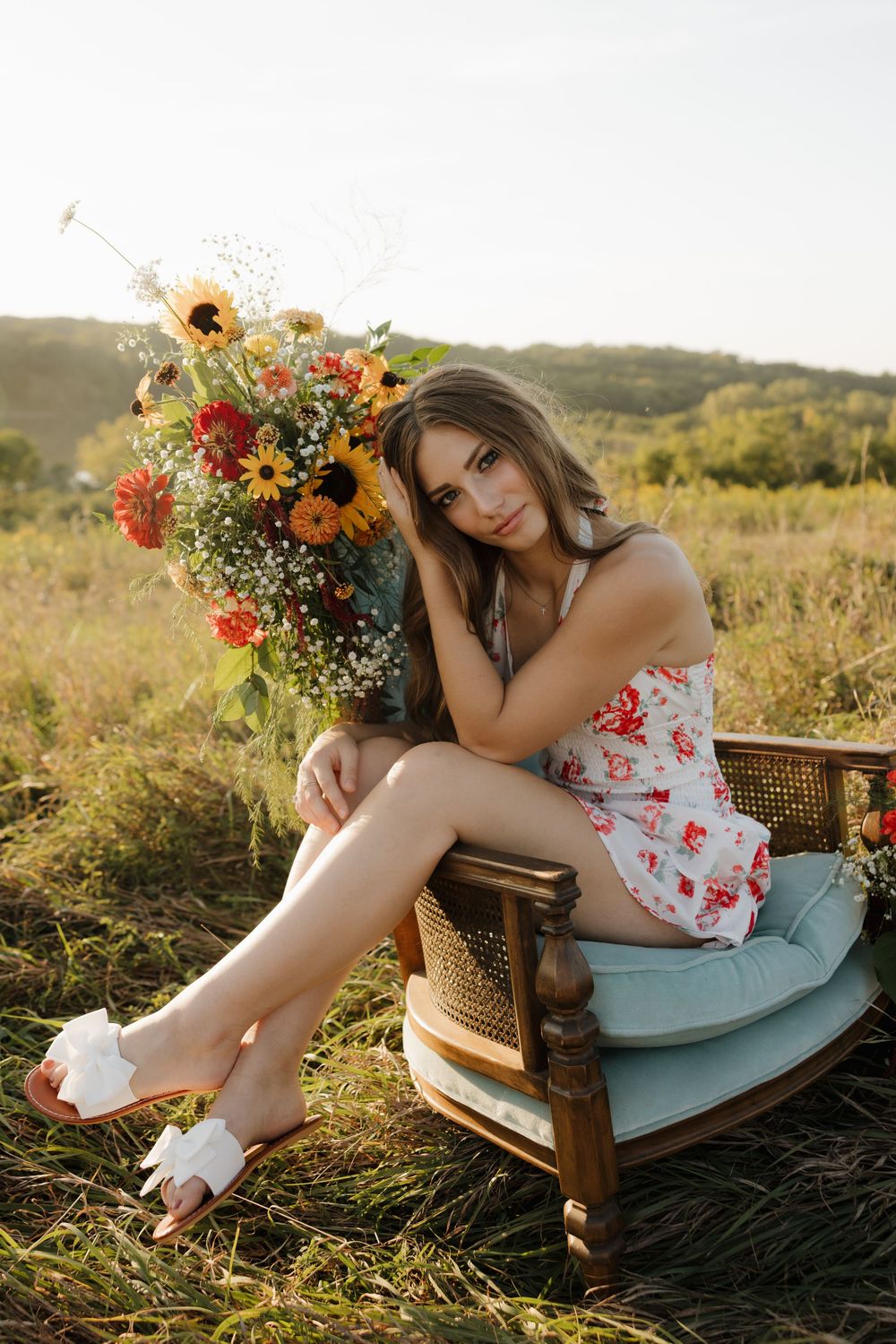 Floral summer photoshoot in a grassy meadow with vintage wicker chair at golden hour.