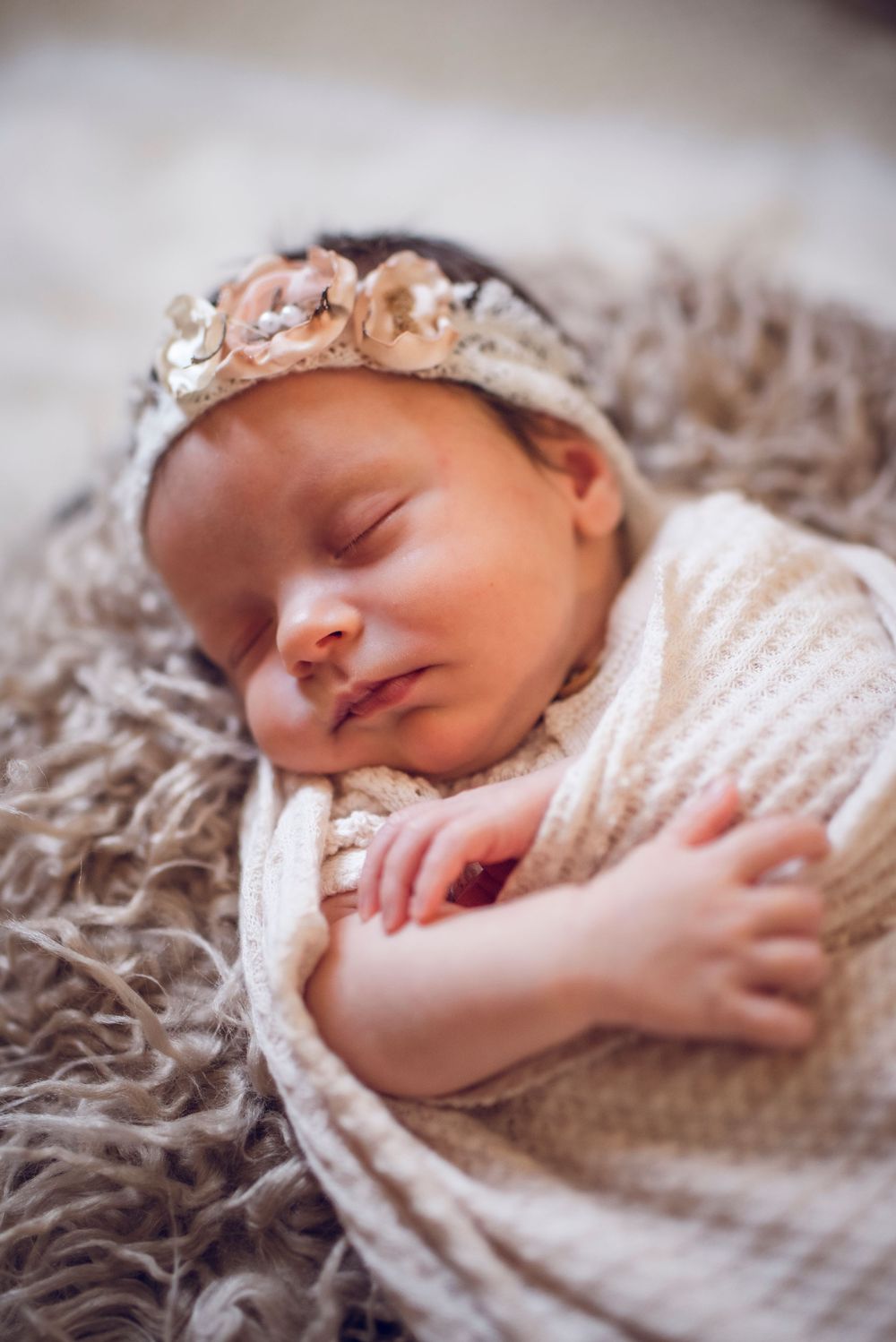 Sleeping newborn baby wrapped in soft white knit blanket resting on textured gray bedding.
