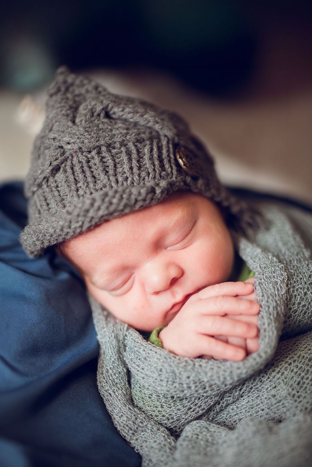 Sleeping newborn baby wrapped in cozy gray knit blanket and matching hat in soft natural lighting.