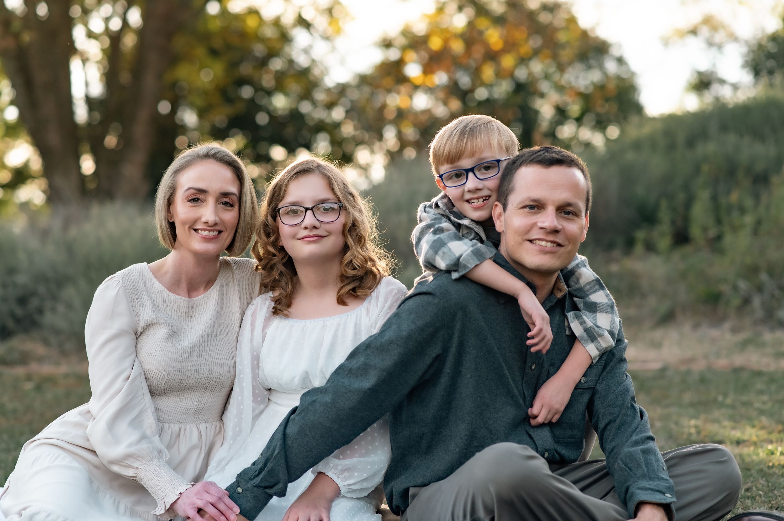 Outdoor family portrait of four people sitting together in casual wear at sunset.