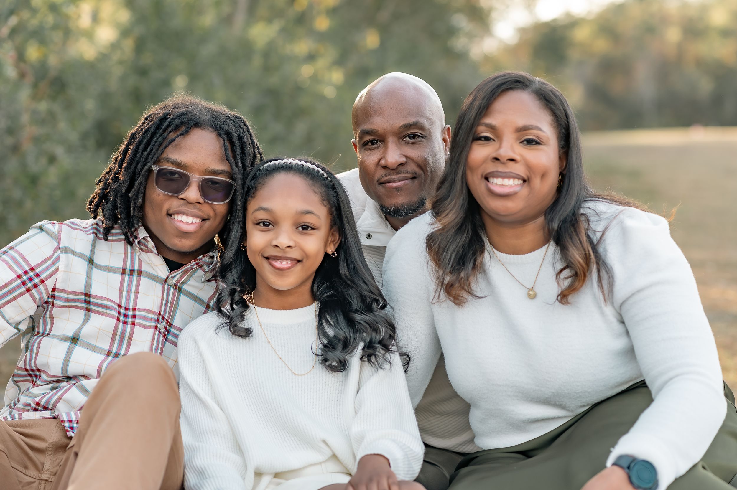 A happy family poses together outdoors during a golden hour photoshoot wearing coordinated white and plaid outfits.