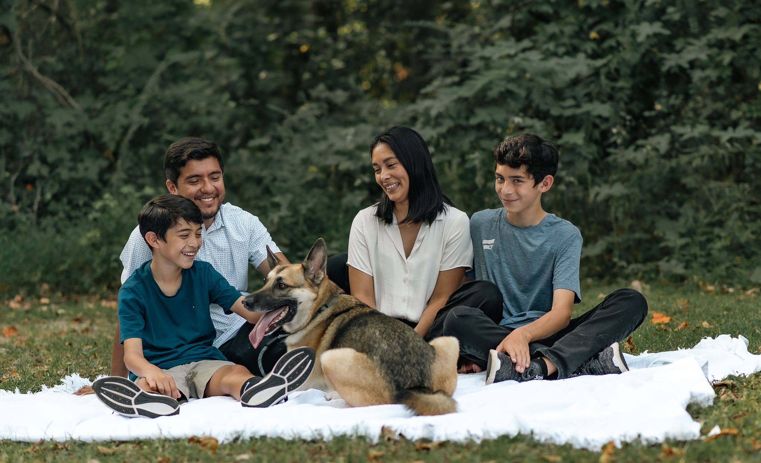Group of teens sitting on blanket outdoors with dog enjoying quality time together.
