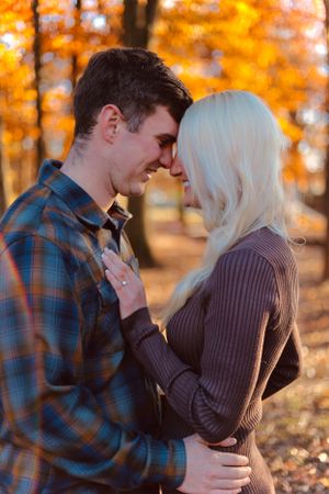 Romantic autumn engagement photo with couple against vibrant orange foliage background.